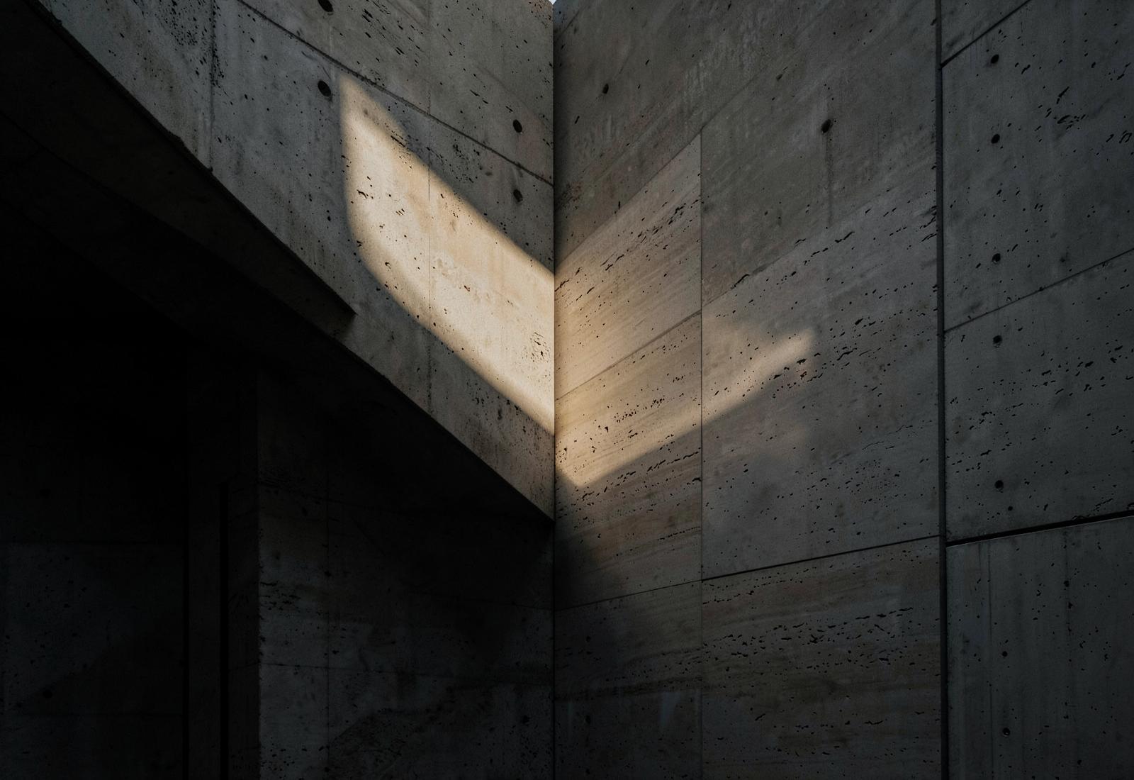 Concrete and travertine architectural planes crossed by a single shaft of warm light